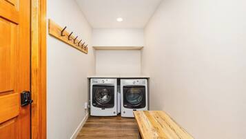 A laundry room with two washing machines, a wooden bench, and a coat rack.
