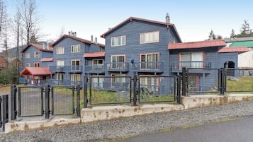 Una hilera de casas azules con balcones, un camino de entrada con portón y un cielo despejado.