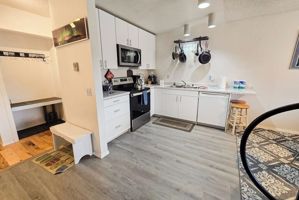 A compact kitchen with white cabinets, a microwave, a stove, and hanging pots.