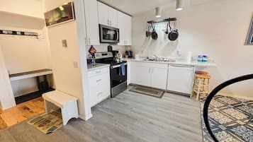 A compact kitchen with white cabinets, a microwave, a stove, and hanging pots.