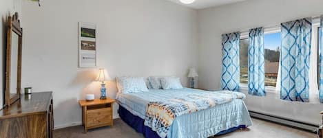 A bedroom with a bed, bedside tables, a lamp, a mirror, and a window with curtains.