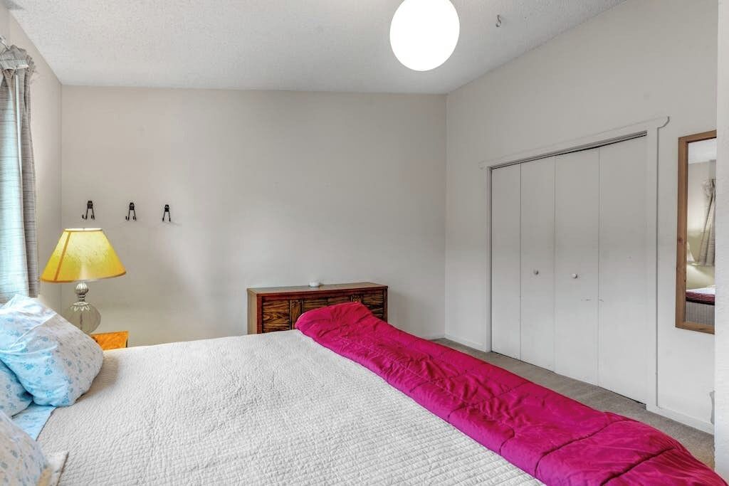 A bedroom with a bed, a bedside lamp, a wooden dresser, and a wardrobe.