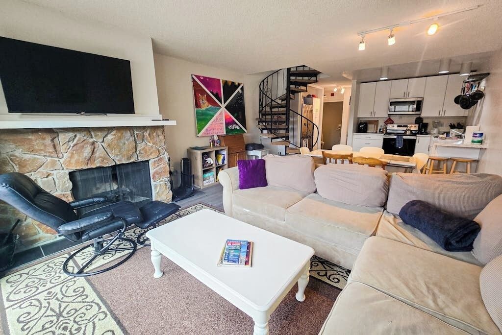 Uma sala de estar com lareira, sofá, mesa de centro e televisão fixada na parede.