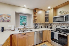 A modern kitchen with wooden cabinets, stainless steel appliances, and a window with a view of greenery. - Mountain Chalet w/ Sauna + Patio 0.5mi to Alyeska (Girdwood)