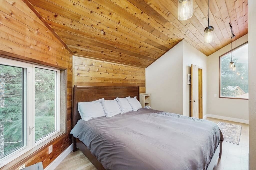 A bedroom with a wooden ceiling, a large bed, a window, and a door.