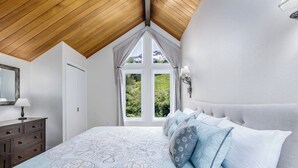 Un dormitorio con una cama grande, un aparador, una ventana con cortinas y vistas a zonas verdes.