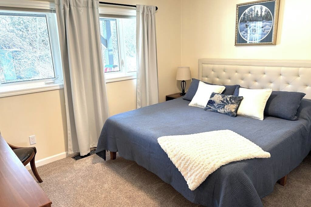 A bedroom with a large bed, a nightstand, a lamp, and a window with curtains.