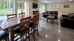 A spacious living room with a dining area, a fireplace, and a ceiling fan. - Lower Level of the Monarch Estate for Smaller Groups (Girdwood)