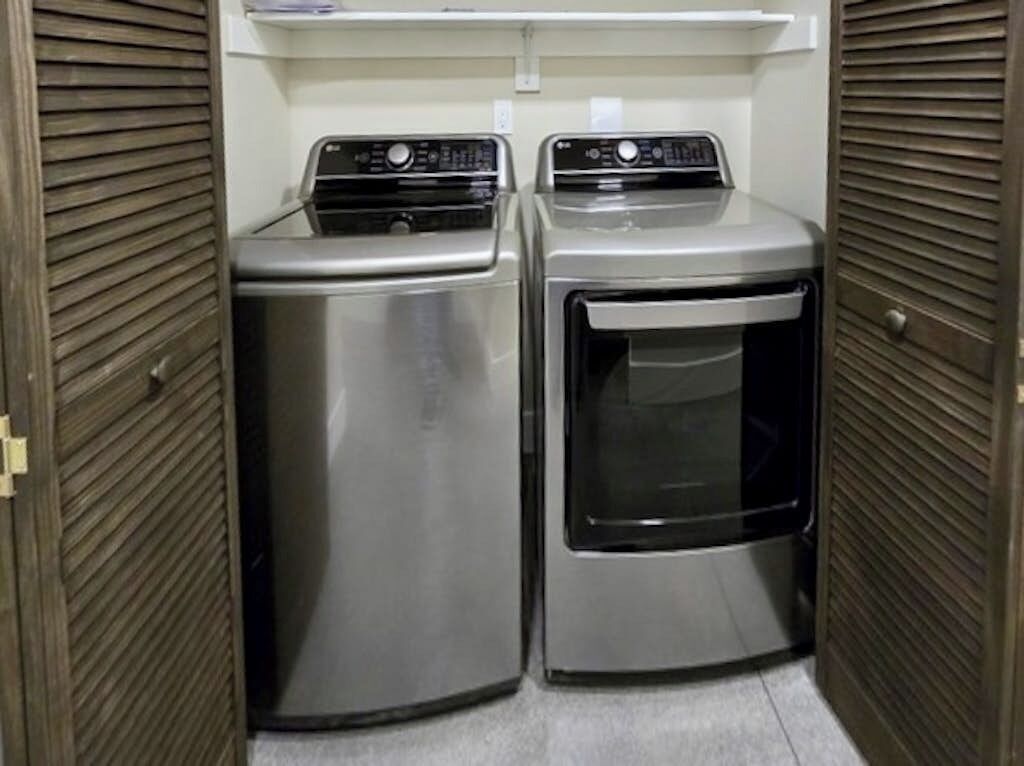 Une buanderie équipée de deux appareils en acier inoxydable, dont un sèche-linge et une machine à laver, le tout dissimulé derrière des portes à persiennes en bois.