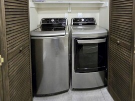 Lavandería con dos electrodomésticos de acero inoxidable: una secadora y una lavadora, todo ello cerrado por puertas de madera con listones.