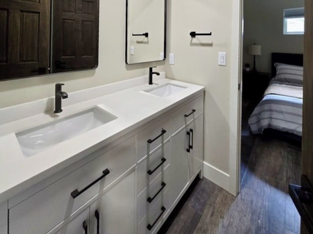 Une salle de bain avec un meuble-lavabo à deux vasques, un miroir et une porte donnant sur une chambre.