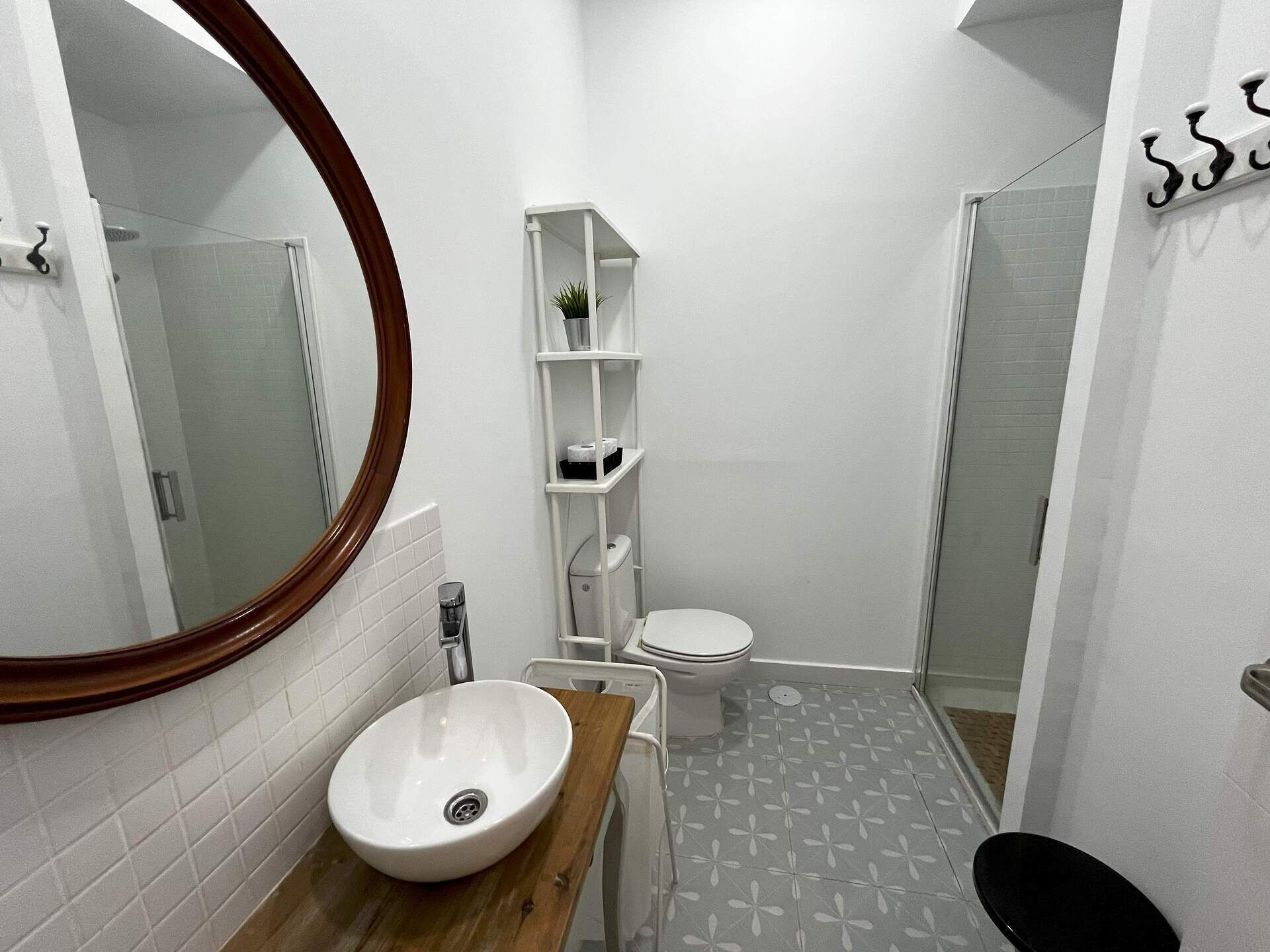 Een badkamer met een ronde spiegel, een wastafel met houten blad, een toilet en een douchehoek.