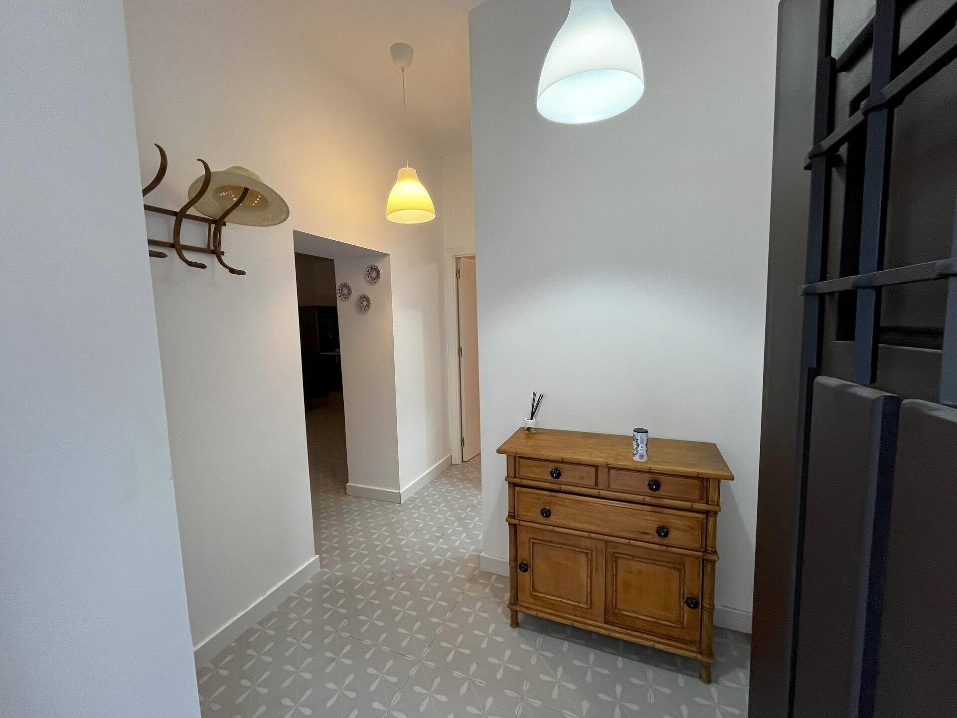 Een hal met een houten dressoir, een hanglamp en een deur met een metalen rooster.