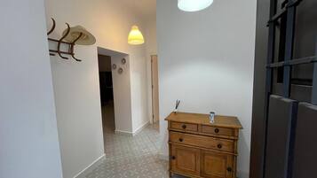 Een hal met een houten dressoir, een hanglamp en een deur met een metalen rooster.