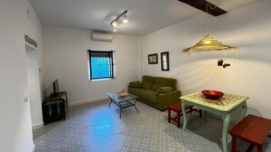 A compact living space with a sofa, a small table with a bowl, a coffee table, and a window with blinds.