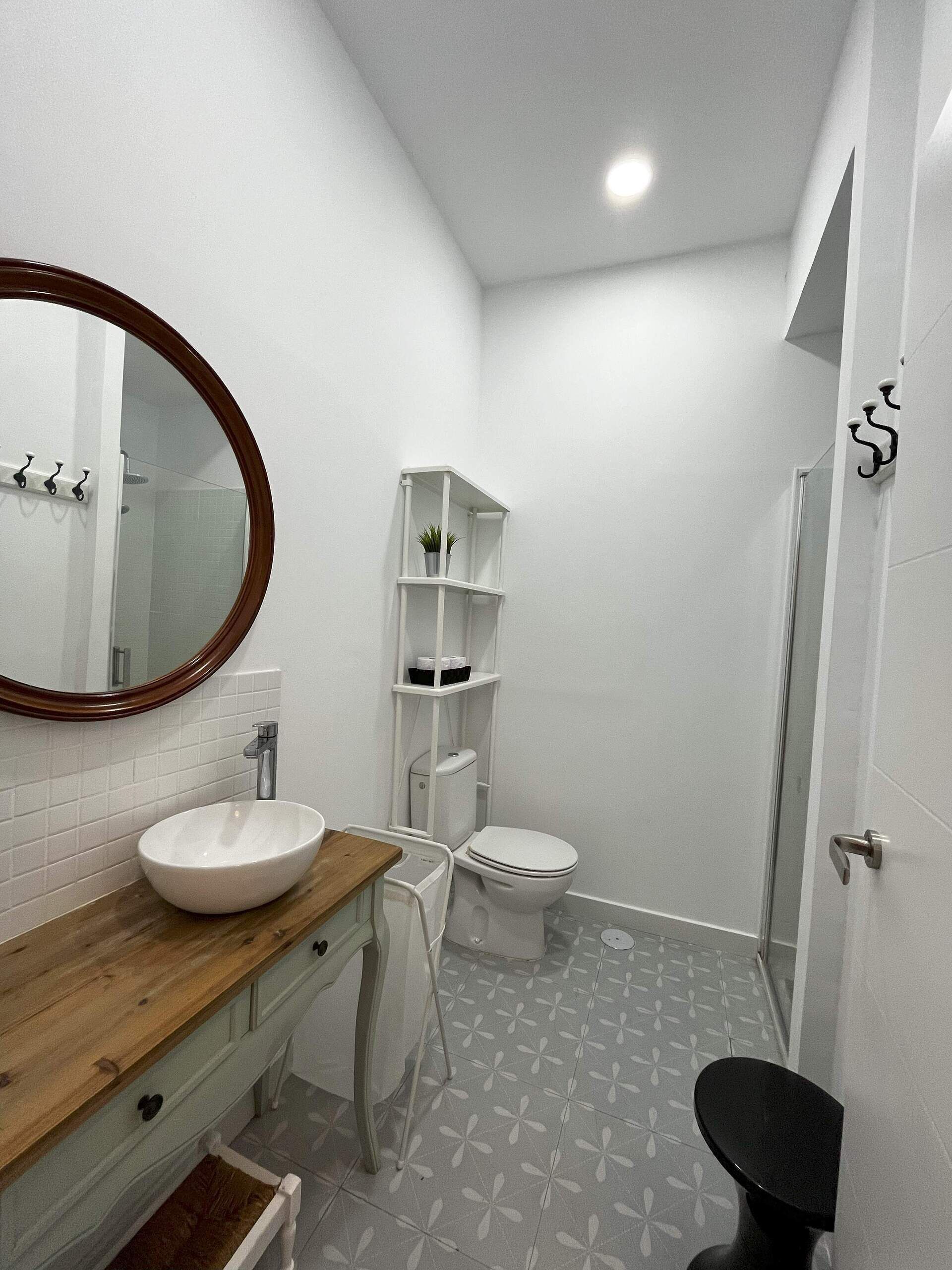 Une salle de bain avec un meuble-lavabo en bois, un lavabo blanc, des toilettes, un espace douche et un sol carrelé de couleur blanche.