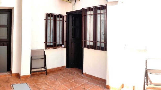 A small, enclosed patio area with tiled flooring, a metal chair, and a door with barred windows.