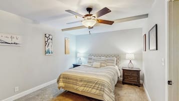 A bedroom with a bed, nightstands, a ceiling fan, and wall art.