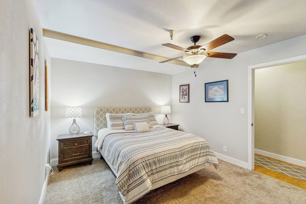 A bedroom with a bed, nightstands, a ceiling fan, and framed pictures on the wall.