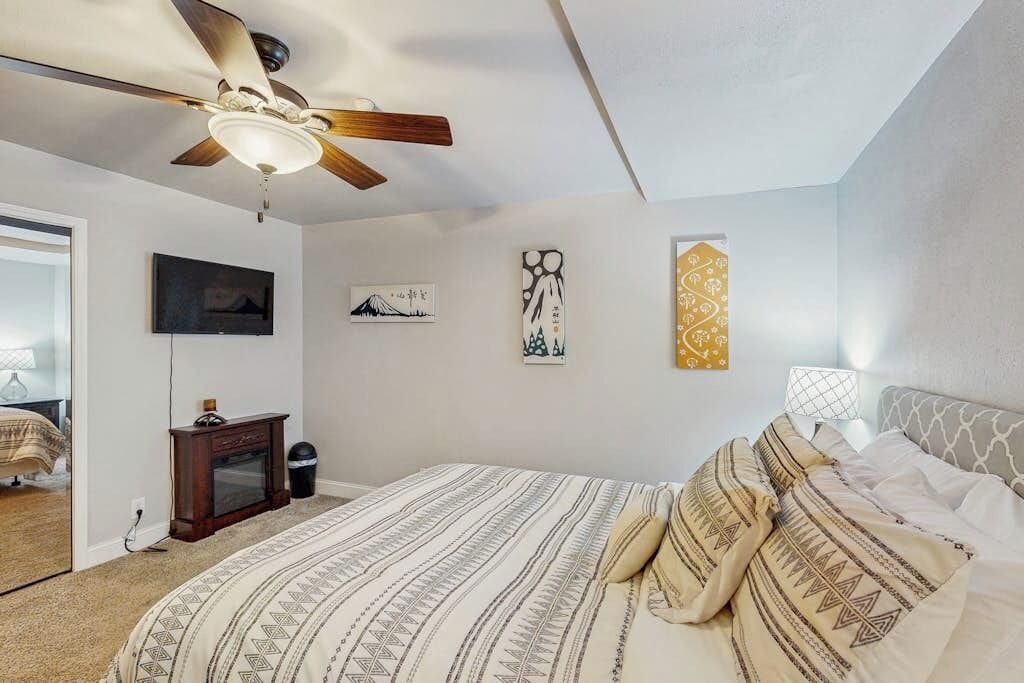 Un dormitorio con cama, ventilador de techo, televisión y obras de arte en las paredes.