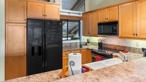 Una cucina con mobili in legno, un frigorifero nero, un forno a microonde, piani di lavoro in granito e una ventola a soffitto.