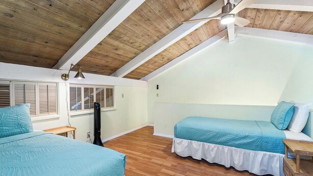 Una camera da letto con due letti, pavimento in legno, ventilatore a soffitto e una finestra con persiane.