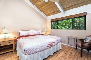 A bedroom with a bed, bedside tables, a desk, and a window with a view of greenery.