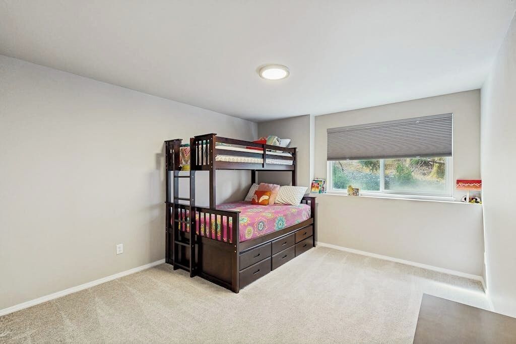 A bedroom with a bunk bed, a window with blinds, and a carpeted floor.