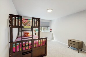 A bunk bed with a lower bunk, a small bedside table, and a window with blinds.