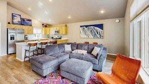 A modern living space with a grey sectional sofa, a vibrant rug, and a mountain painting.