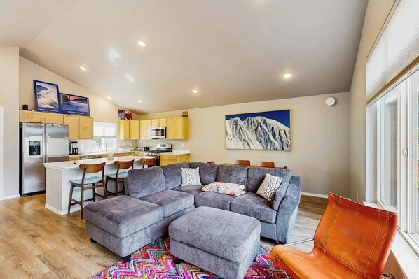 A modern living space with a grey sectional sofa, a vibrant rug, and a mountain painting. - Cozy Mountainside Duplex Near Virgin Creek Trailhead (Girdwood)