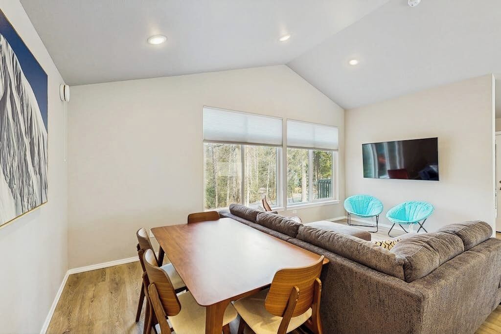 A modern living room with a wooden dining table, a sofa, and two blue chairs.