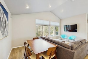 A modern living room with a wooden dining table, a sofa, and two blue chairs. - Cozy Mountainside Duplex Near Virgin Creek Trailhead (Girdwood)