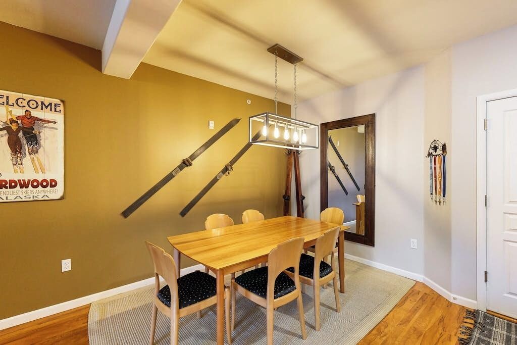 A dining area with a wooden table and chairs, a hanging light fixture, and a poster on the wall.