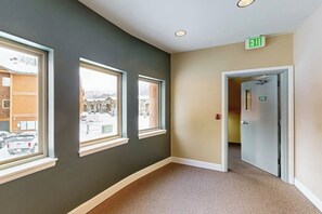 A hallway with a carpeted floor, a door with an exit sign, and windows with a view of a snowy landscape.