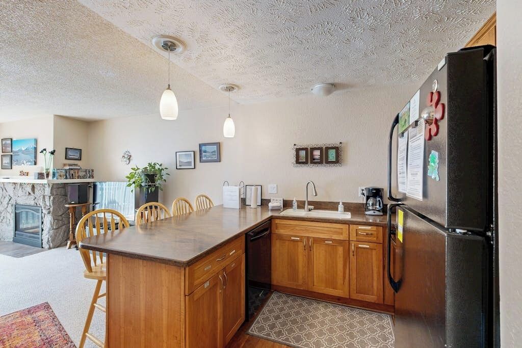 A kitchen with wooden cabinets, a black refrigerator, and pendant lighting.