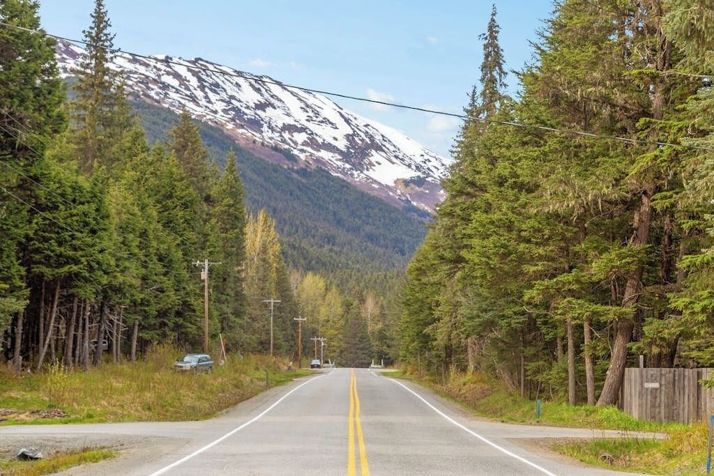 Uma estrada de duas pistas ladeada por florestas densas e uma montanha nevada ao longe.