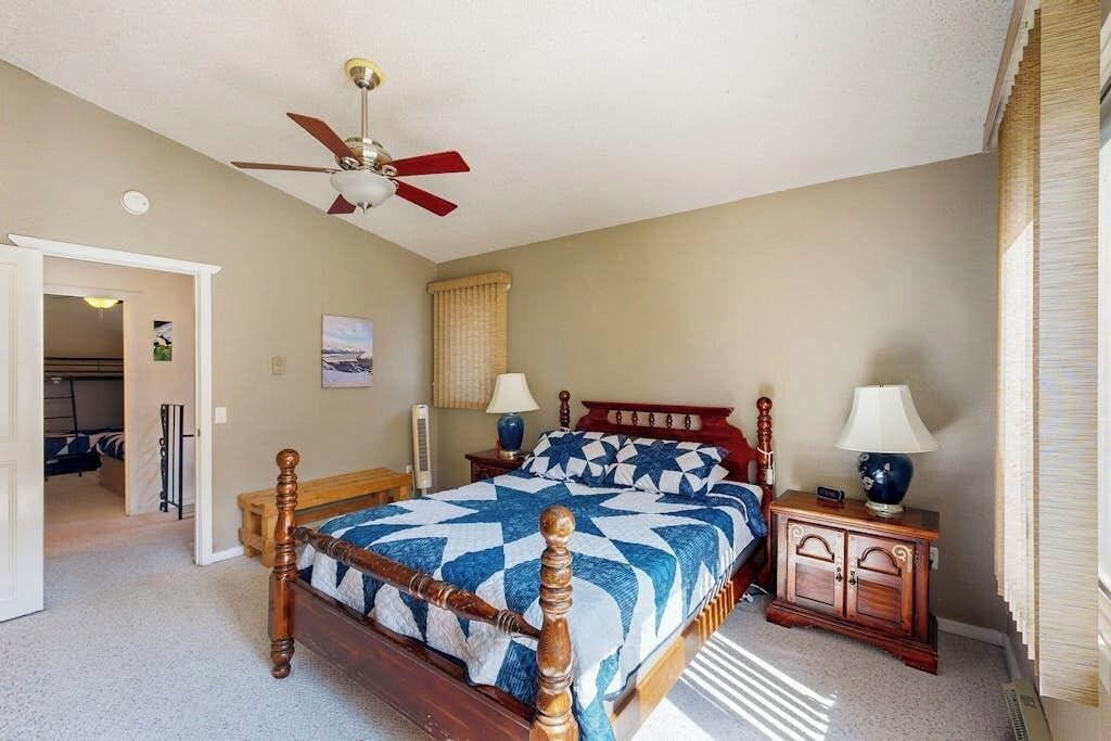 A bedroom with a wooden bed, two bedside tables, a ceiling fan, and a door leading to another room.