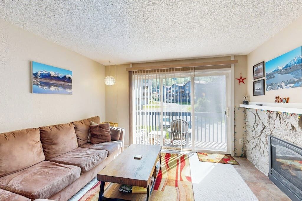 A living room with a sofa, a coffee table, and a fireplace. There is a sliding glass door leading to an outdoor area.