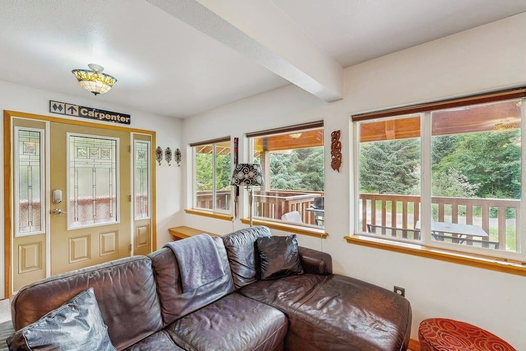 A room with a leather couch, a sign indicating a carpenter's room, and large windows with a view of trees.