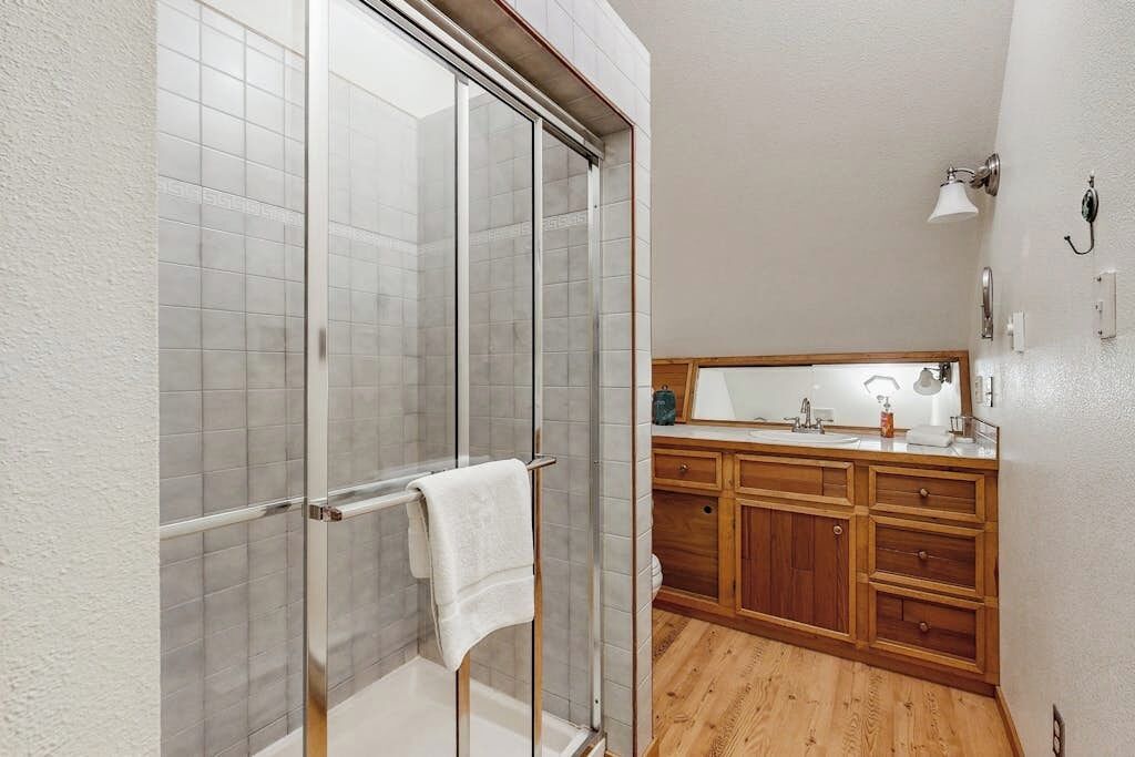 A bathroom with a glass shower enclosure, wooden cabinets, and a mirror above the sink.