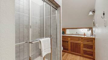A bathroom with a glass shower enclosure, wooden cabinets, and a mirror above the sink.