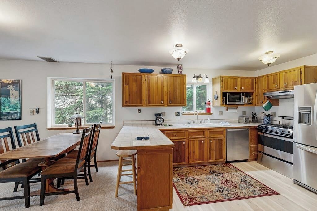 A kitchen with wooden cabinets, a stainless steel refrigerator, and a dining area with a table and chairs.