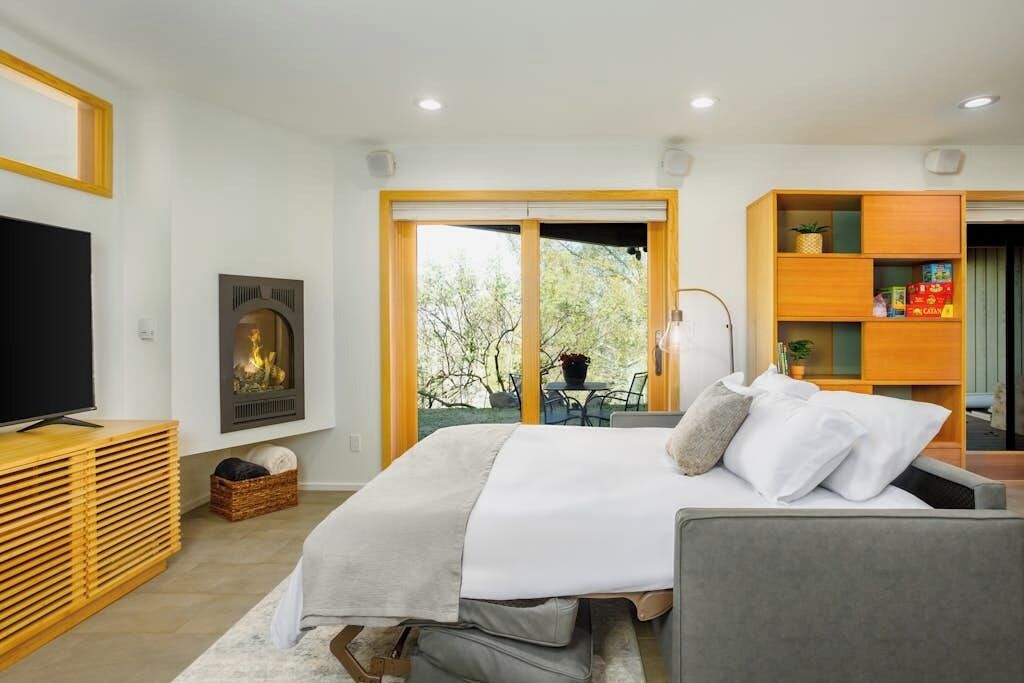 Quarto com cama, televisão, lareira e vista para o exterior.