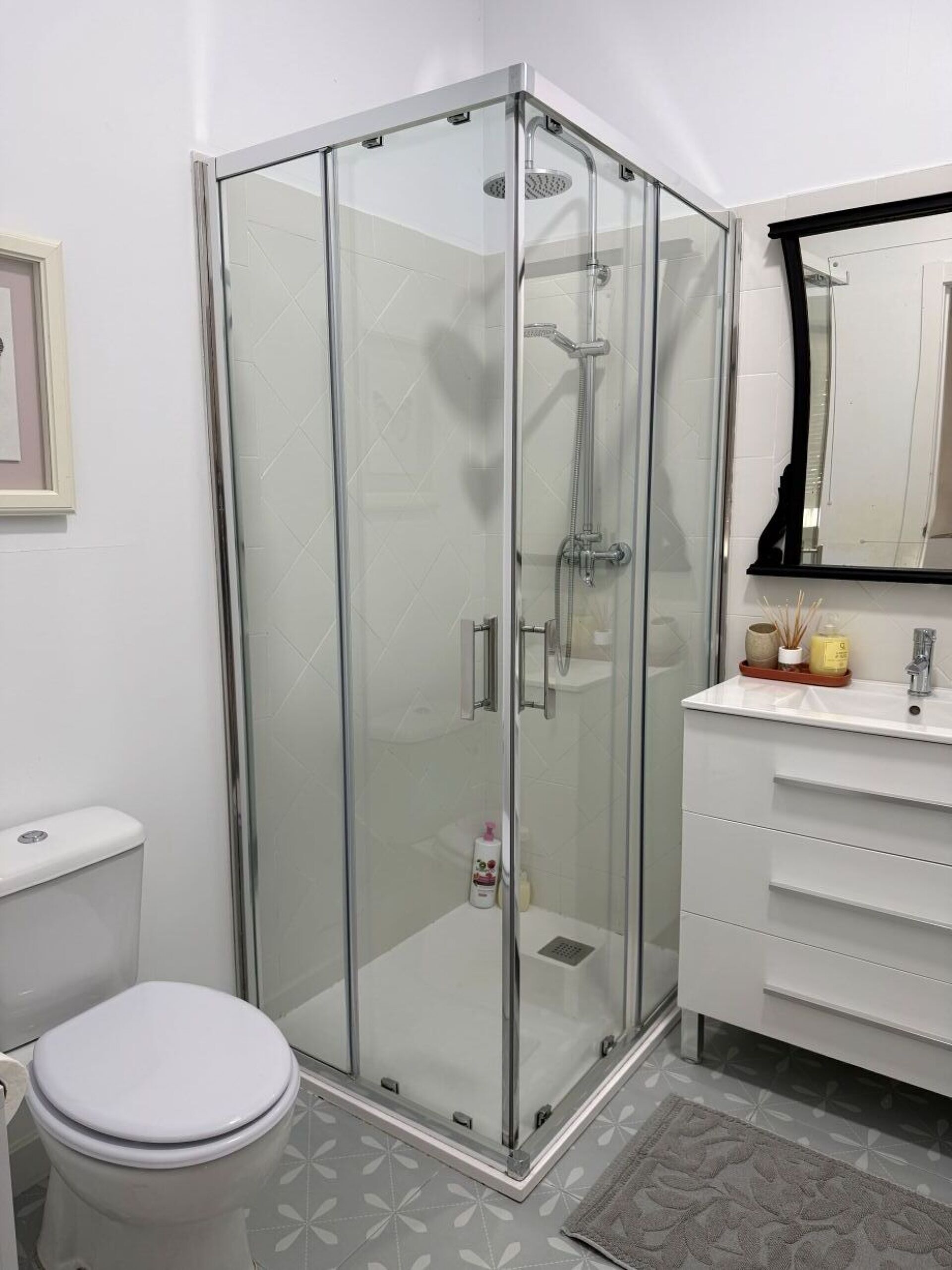 Un baño moderno con ducha de vidrio, inodoro blanco y tocador con espejo.