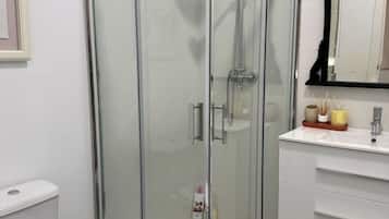 Un baño moderno con ducha de vidrio, inodoro blanco y tocador con espejo.
