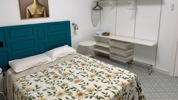 A bedroom with a teal headboard, a bed with floral bedding, a white dresser with drawers, and a wall-mounted mirror.