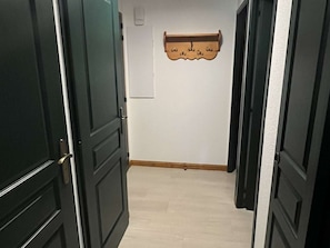 Een hal met donkere houten deuren, een lichtgekleurde vloer en een houten kapstok aan de muur.