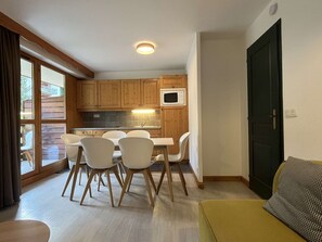 A compact kitchen with wooden cabinets, a dining table with chairs, a microwave, and a large window. - Apartment with parking - 6 guests (Valloire)