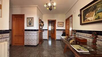 A hallway with a tiled floor, wooden doors, a dining table with a vase, and a ceiling light fixture.